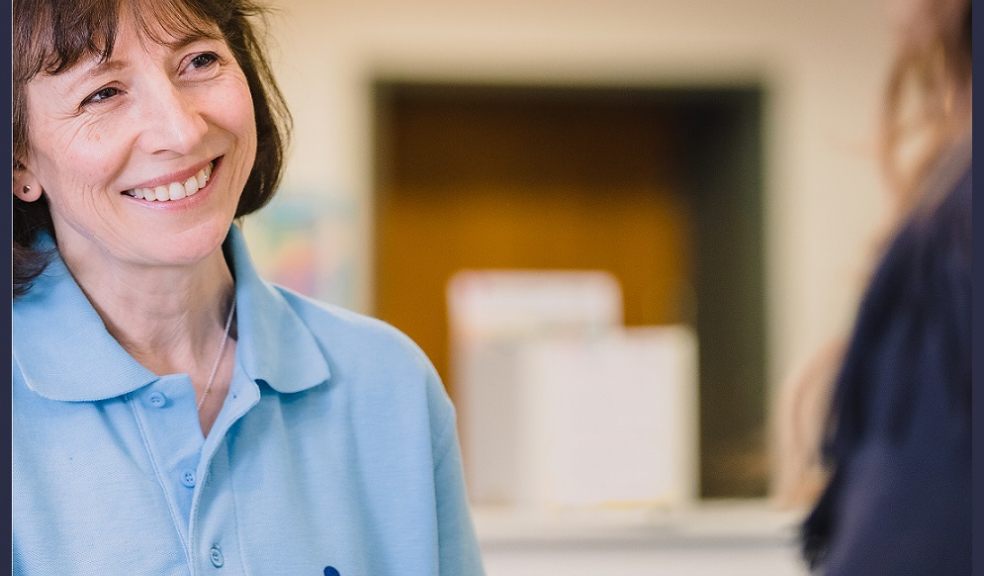 A smiling woman in a blue Guide Dogs tee looks past the camera. 