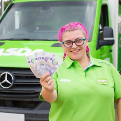 Woman with pink hair holding money in front of an Asda supermarket van