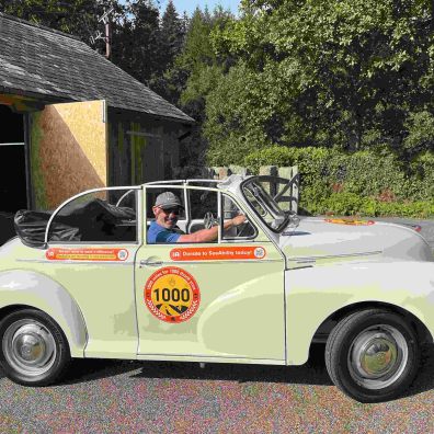 A man sits in the driving seat of a white vintage car